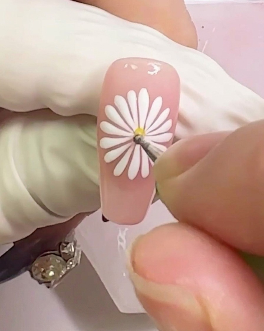 Uno scatto ravvicinato che mostra un punto di gel giallo applicato al centro del design della margherita bianca.