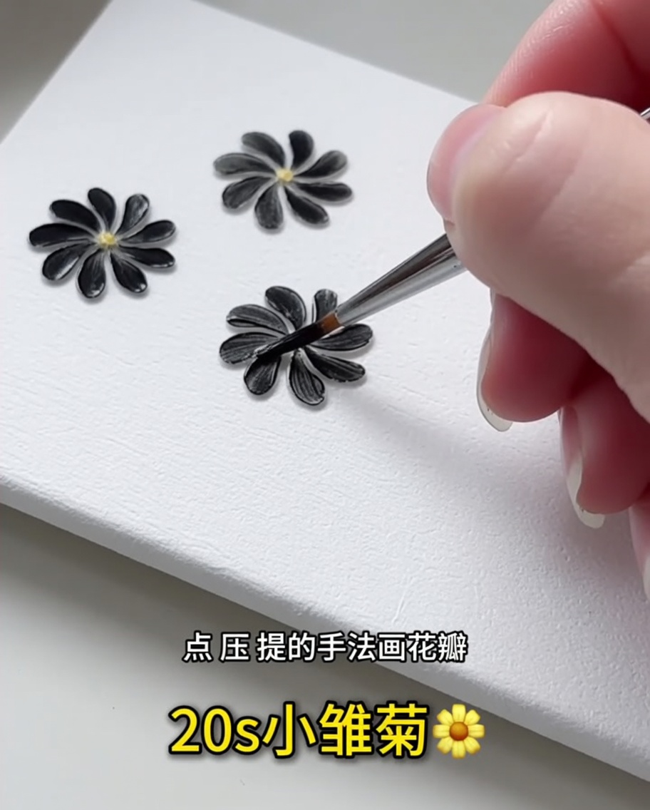 Primo piano di un pennello liner fine che applica un singolo petalo in gel nero su una superficie bianca.