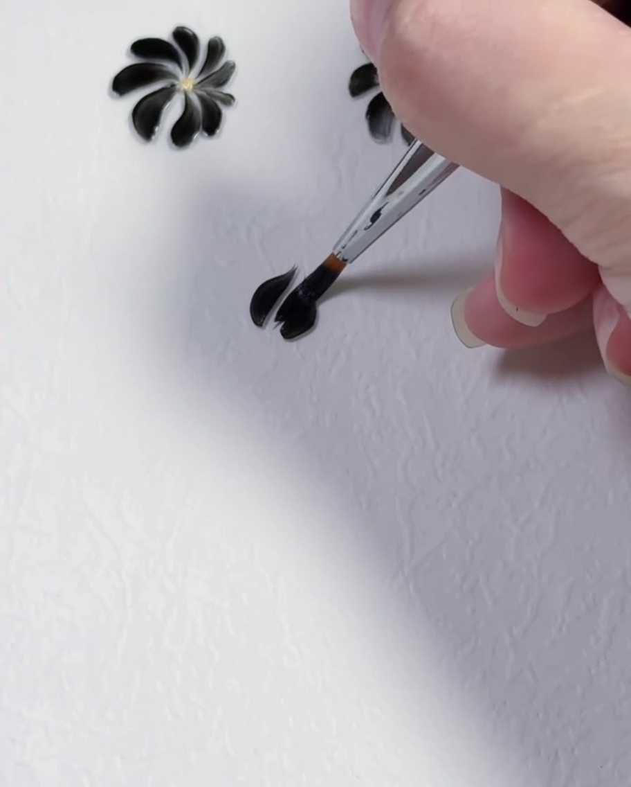 Un pennello liner che crea il secondo petalo in gel nero su sfondo bianco.