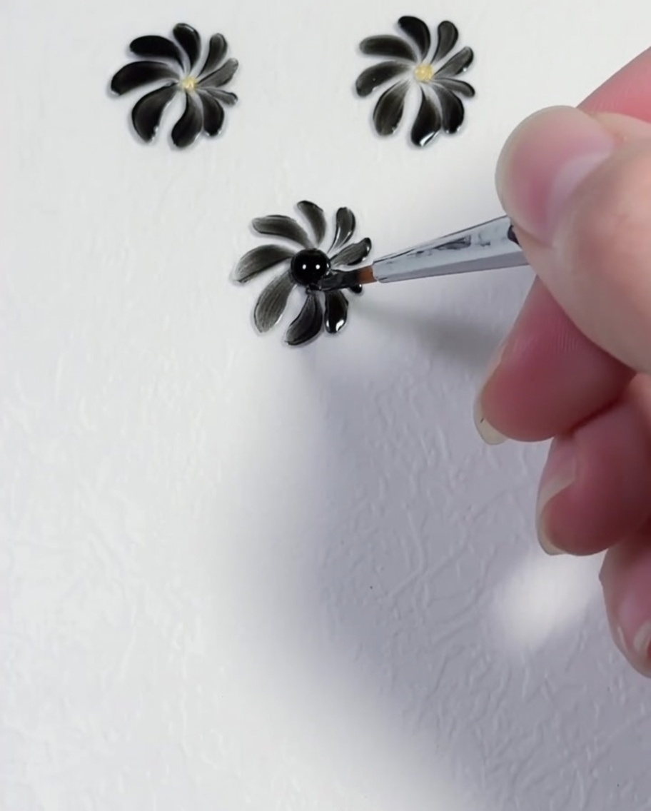 Un dotting tool che posiziona un preciso punto giallo al centro di una margherita nera.