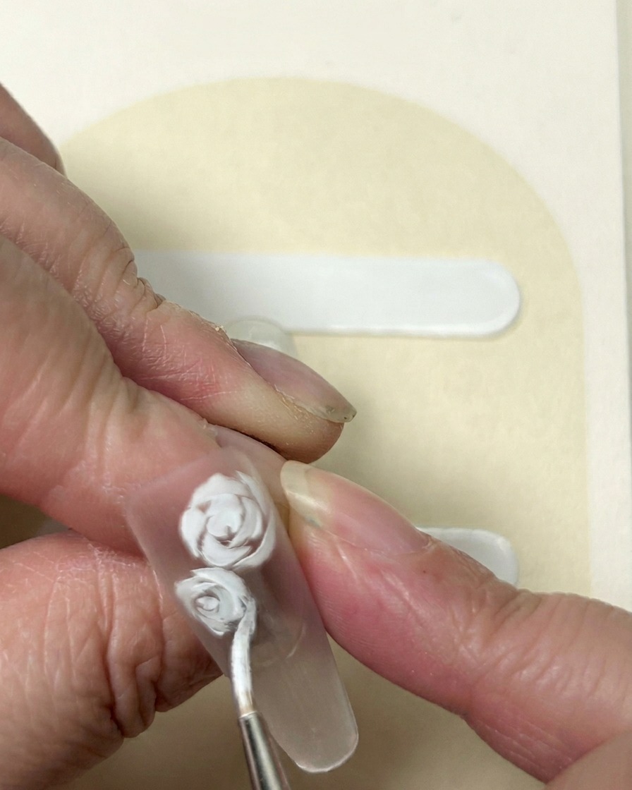 Primo piano di un fiore a cinque petali dipinto in gel bianco accanto a un design di rosa già esistente.