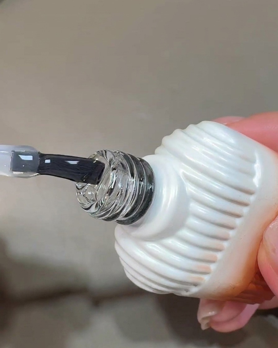 Un pennello applica uno strato trasparente e lucido di blooming gel sulla superficie dellunghia.