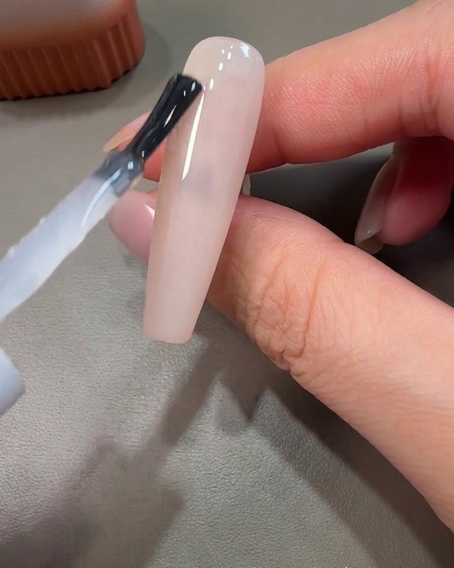 Dettaglio di un pennello liner che applica gel rosa con movimenti circolari su una base non polimerizzata.