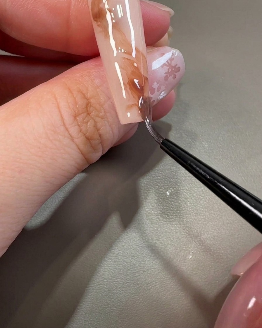 Un pennello liner tira attraverso il gel marrone per creare texture vorticose simili al marmo.