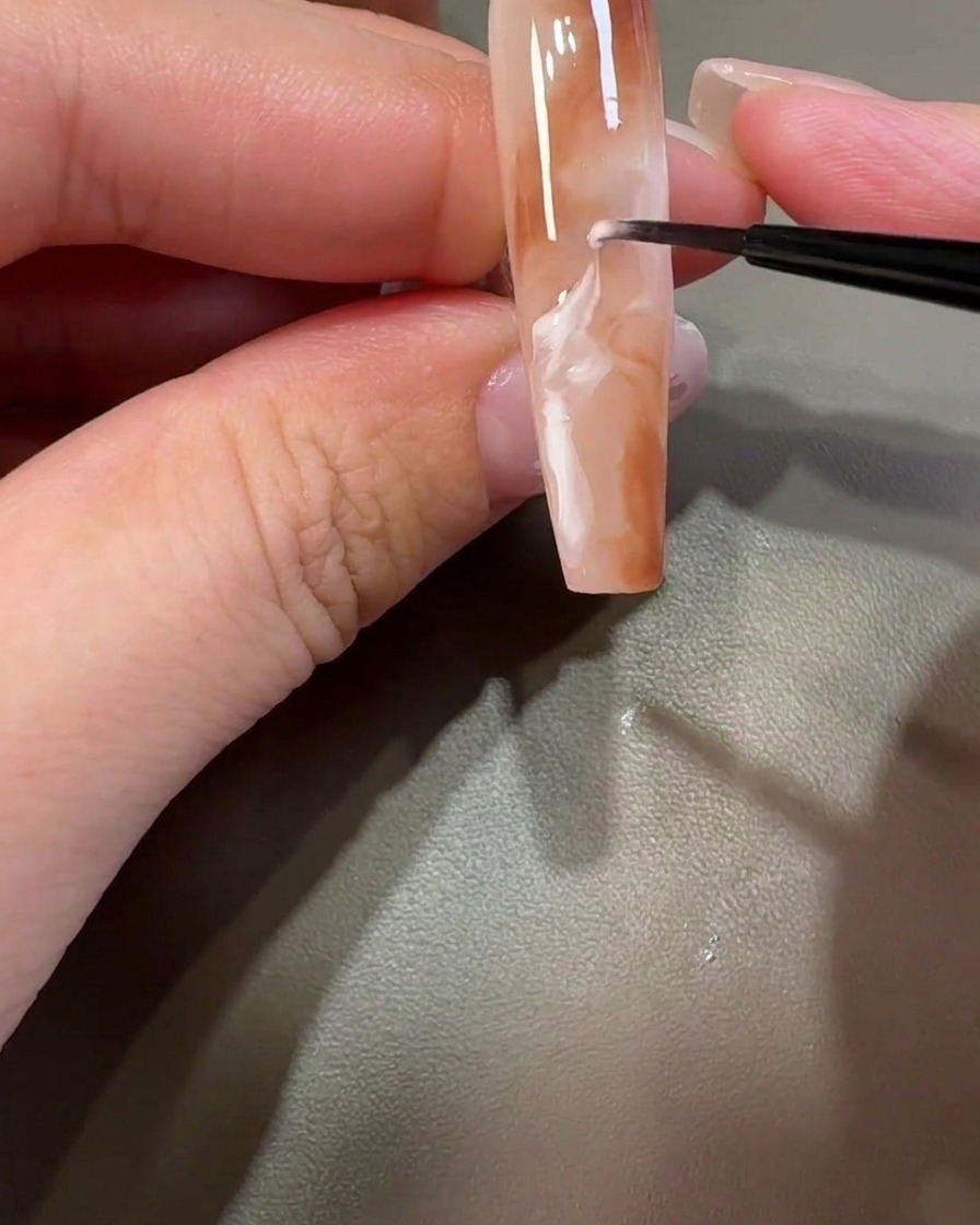 Un pennello liner sfuma il gel bianco attraverso il design marrone per creare motivi marmorizzati.