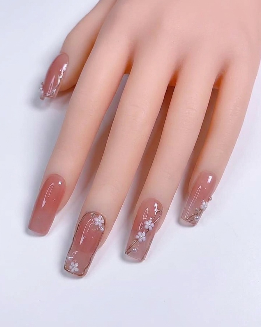 Primo piano di un pennello a punta sottile che applica linee sottili in argento metallizzato su ununghia gel color nude.