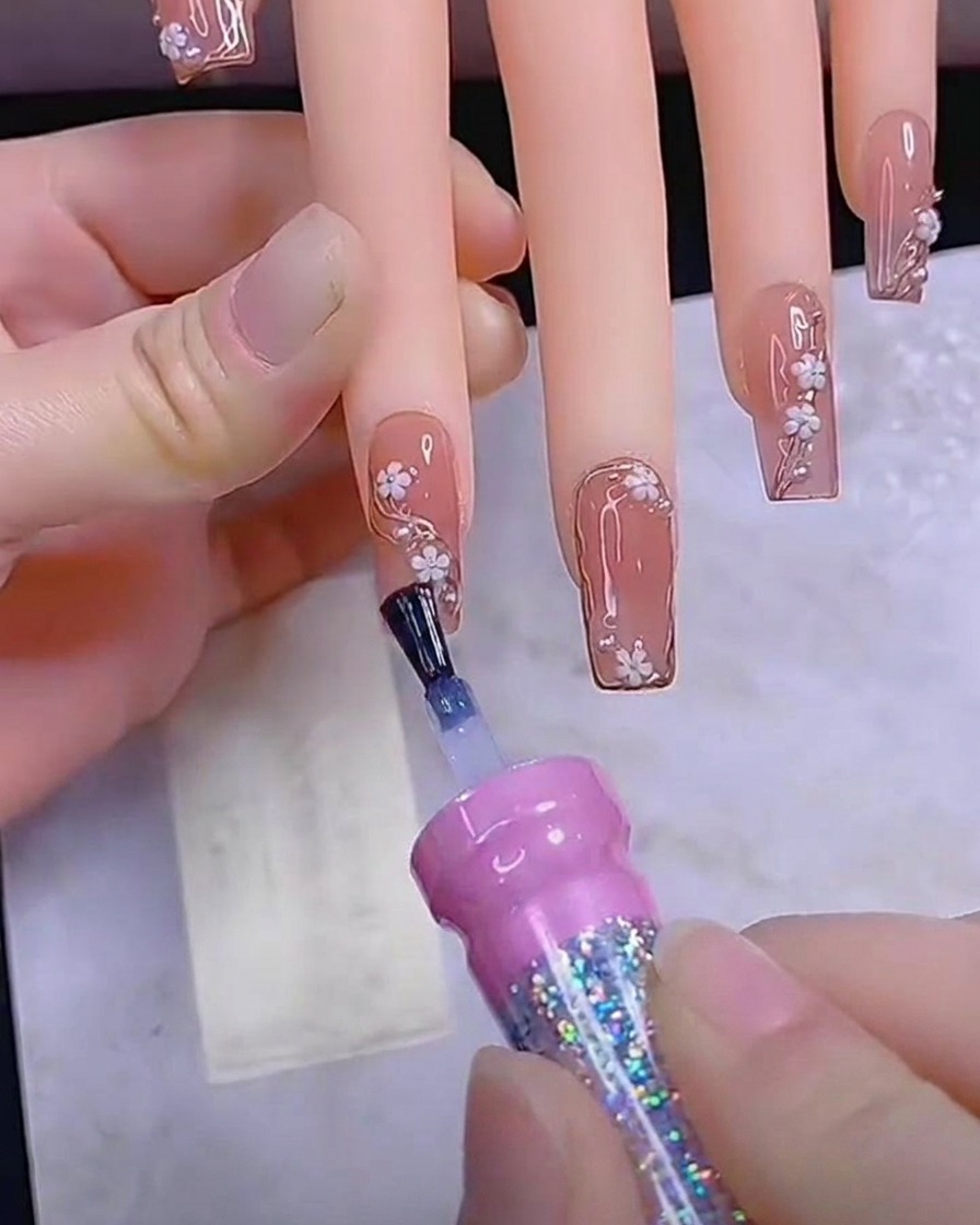Un pennello applica un ultimo strato liscio di top coat lucido su ununghia completamente decorata.