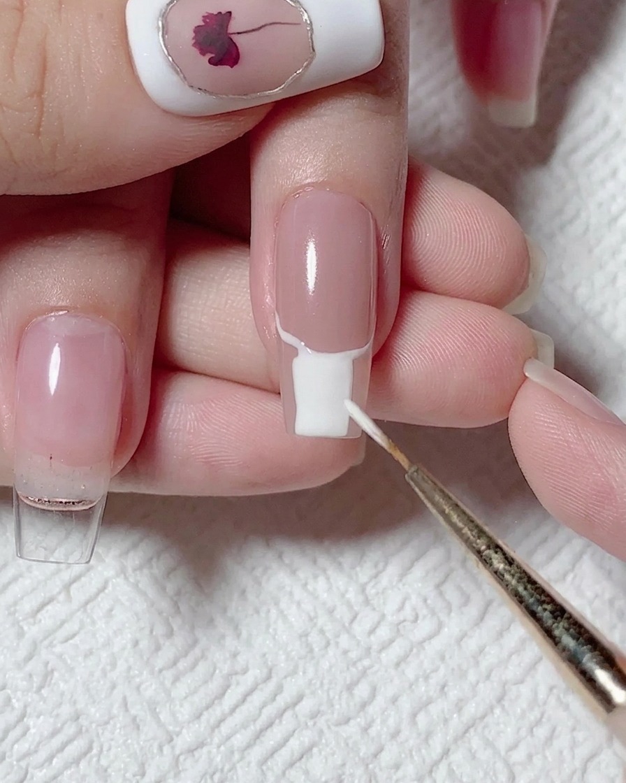Un pennello piatto che riempie la parte inferiore dellunghia con smalto gel bianco coprente.