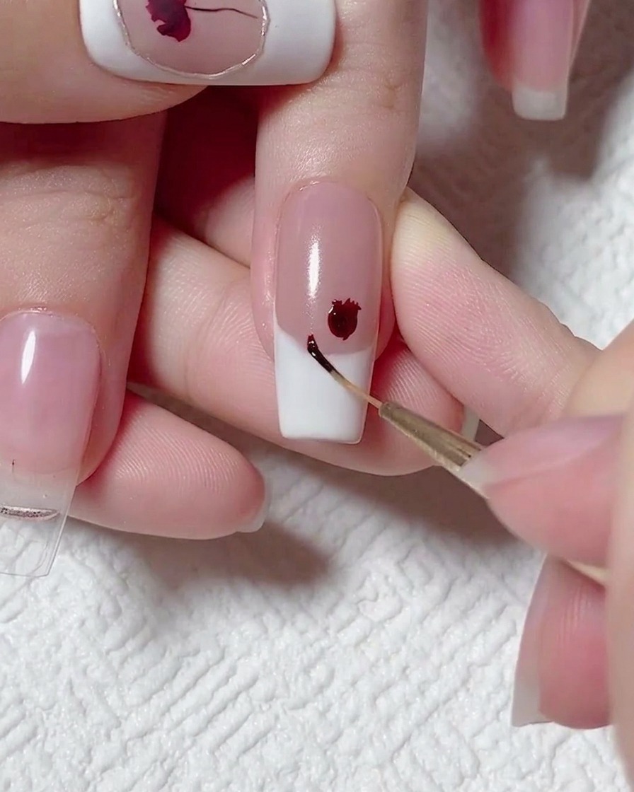 Primo piano di un pennello liner che applica un piccolo punto di gel rosso scuro accanto al fiore principale.