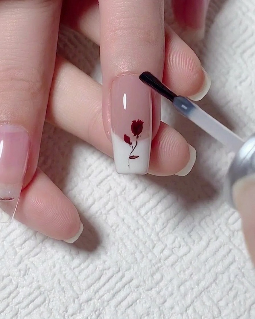 Applicazione di uno strato di top coat opaco sopra ununghia con decorazione a rosa.