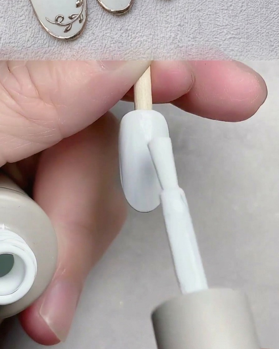 Un pennello applica uno smalto gel bianco liscio sullunghia.