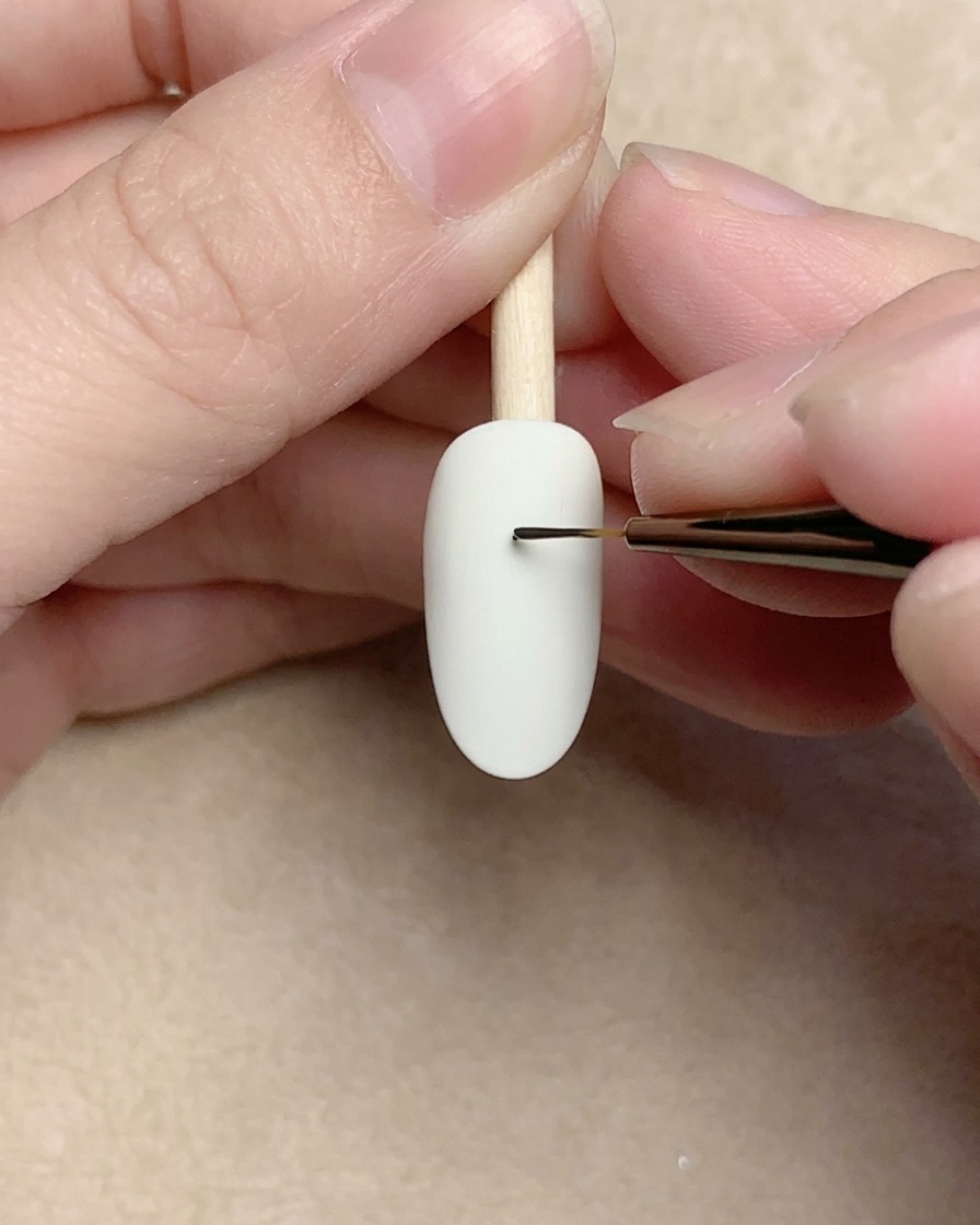 Primo piano di un pennello da nail art che disegna una piccola spirale nera su una base bianca.