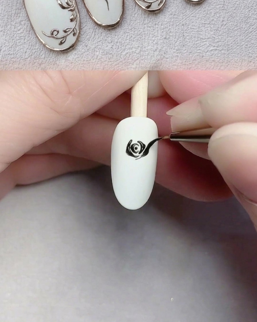 Un pennello da nail art che dipinge grandi petali neri su ununghia bianca per completare una rosa.