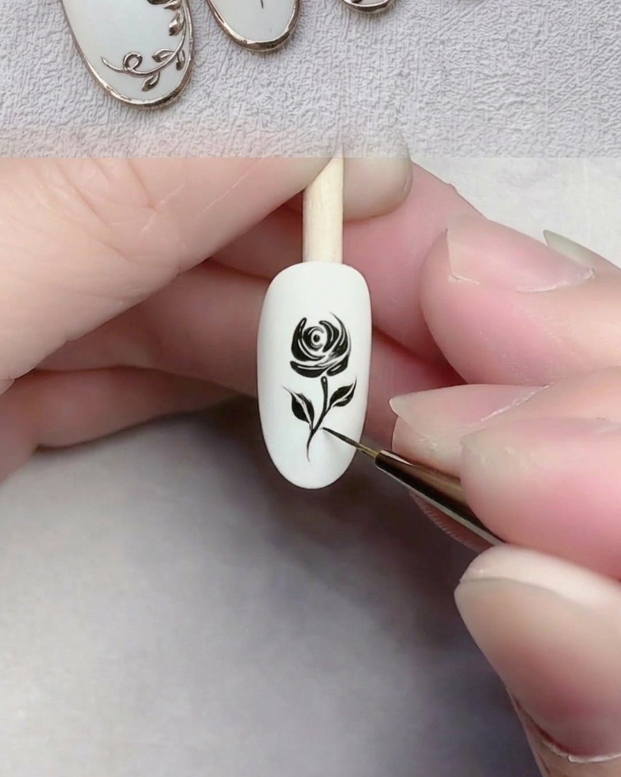 Primo piano di un pennello a punta fine che disegna una linea nera sottile che rappresenta uno stelo su ununghia con base gel bianca.