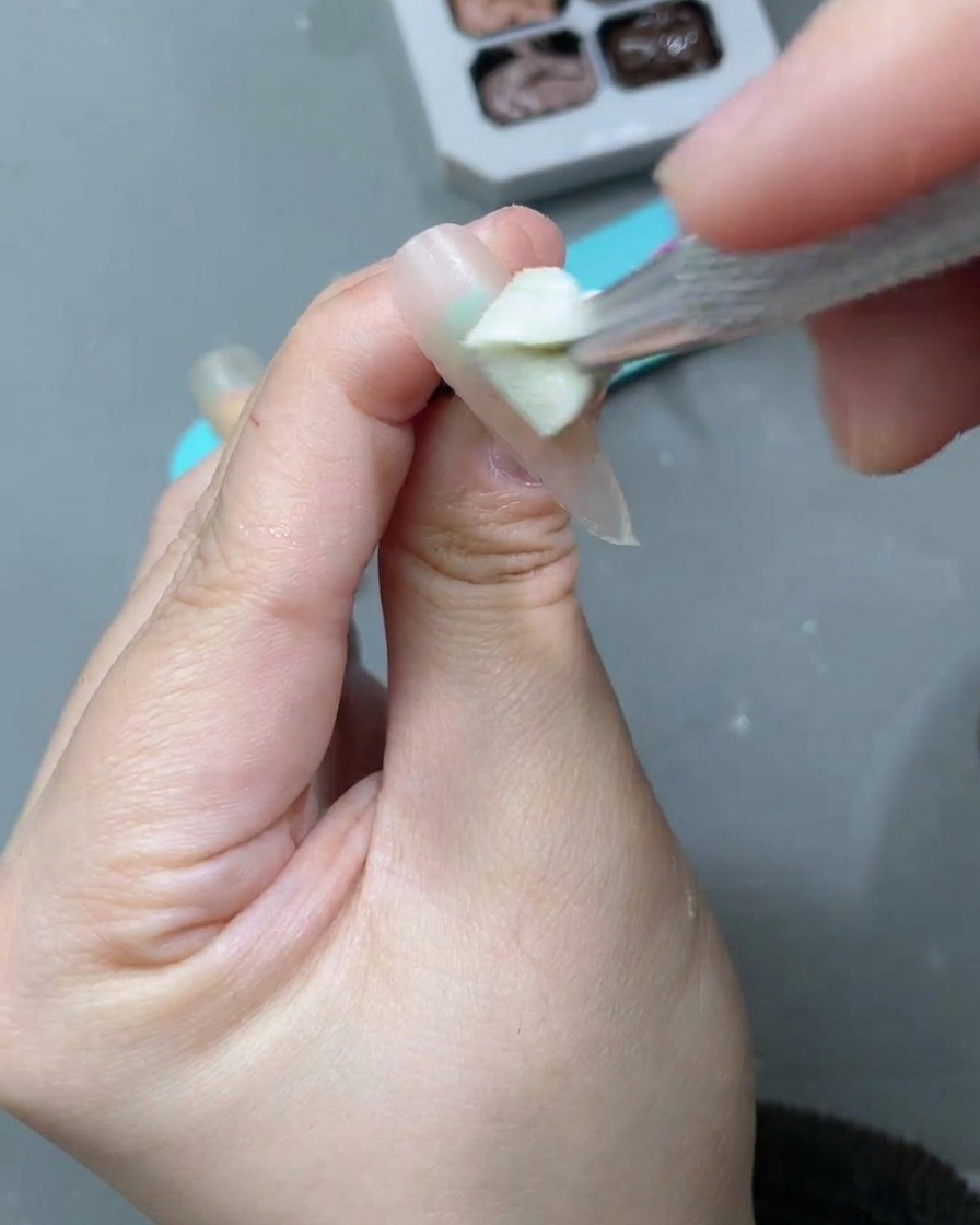 Un pennello che applica un gel cat-eye bianco lunare sopra la base nude precedentemente applicata.