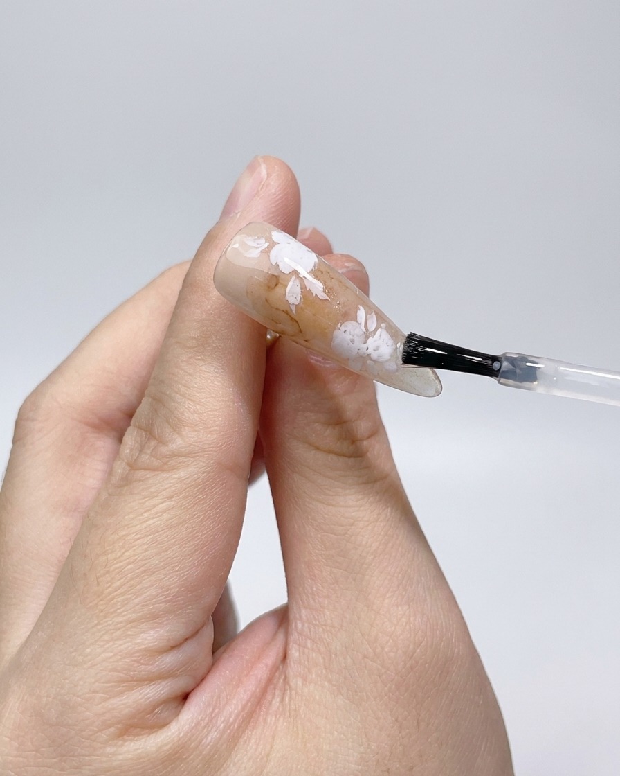 Applicazione di un top coat opaco sopra i contorni di rose bianche sullunghia.