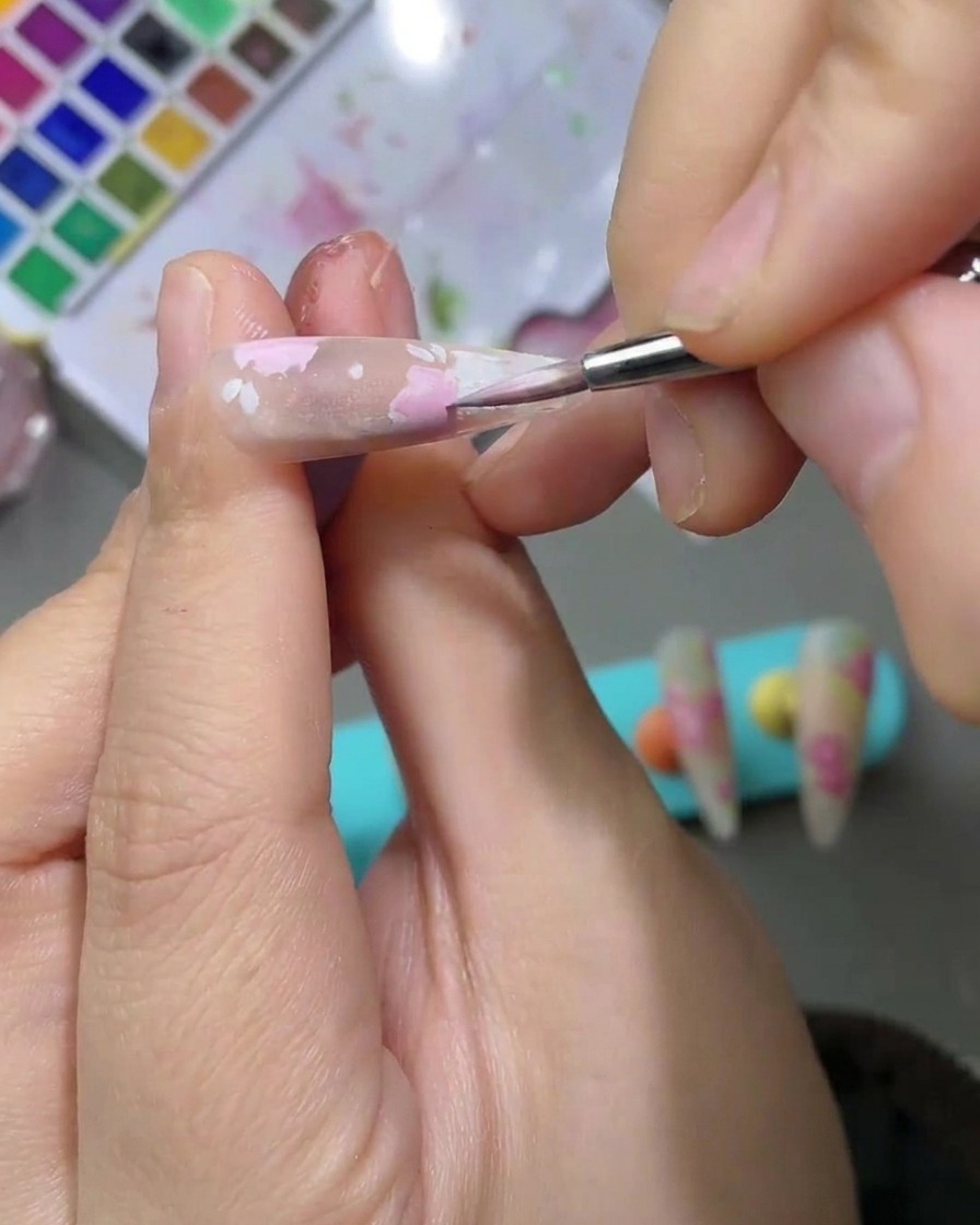Una vista dettagliata di un design nail art con foglie ad acquerello verde chiaro dipinte accanto ai petali di rosa rosa.