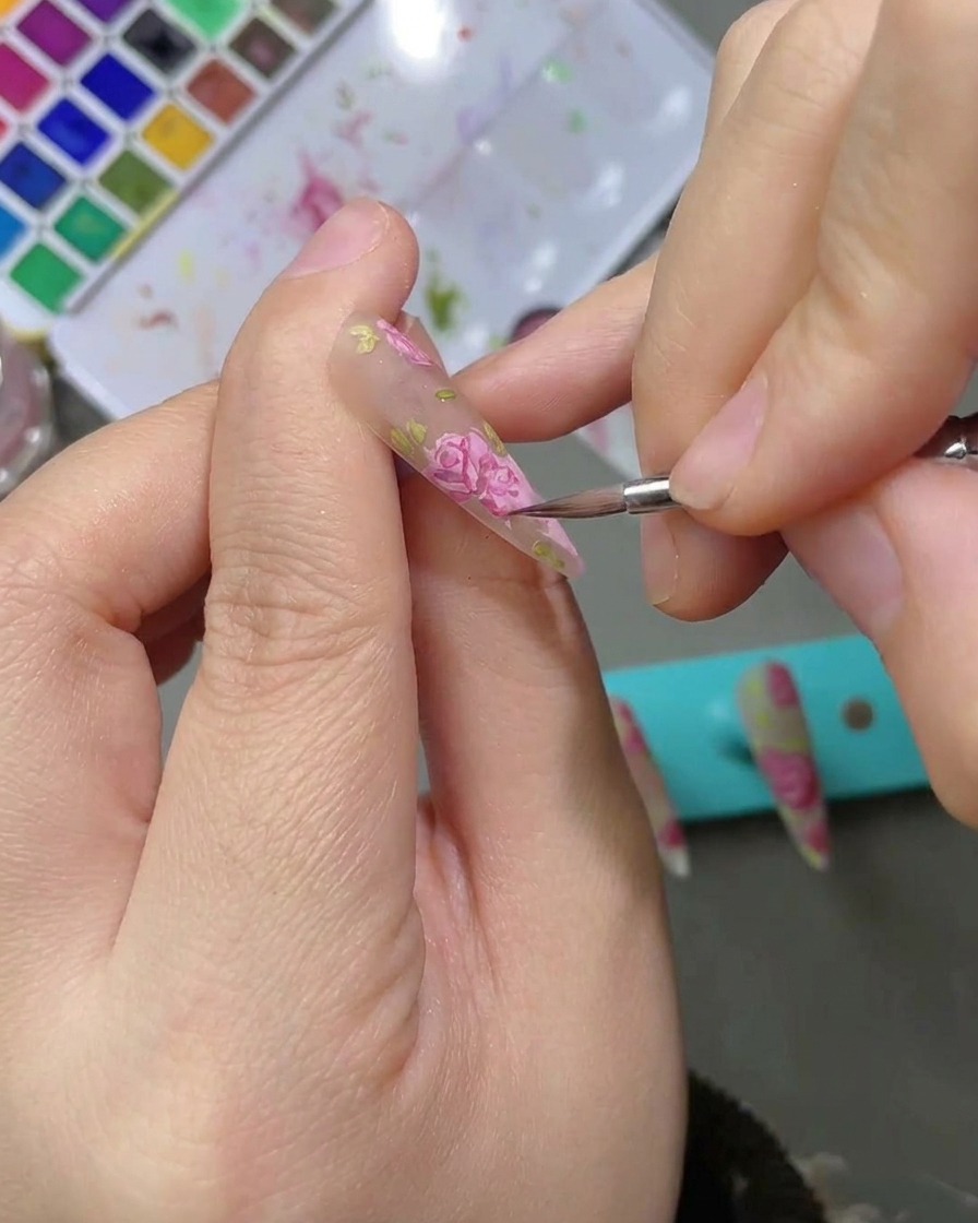 Lapplicazione di un top coat opaco sopra un design per unghie finito e dettagliato con rose ad acquerello.