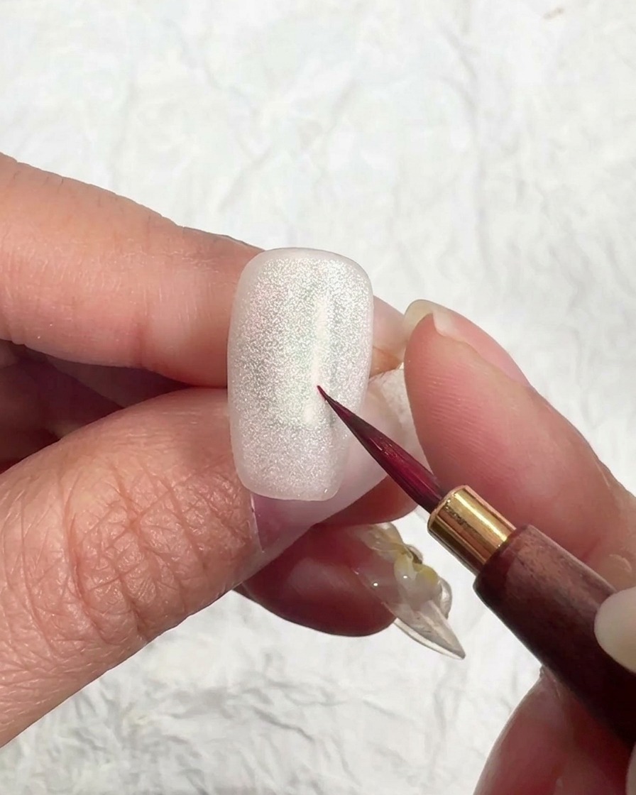 Un pennello applica un top coat opaco su ununghia cat eye brillante.