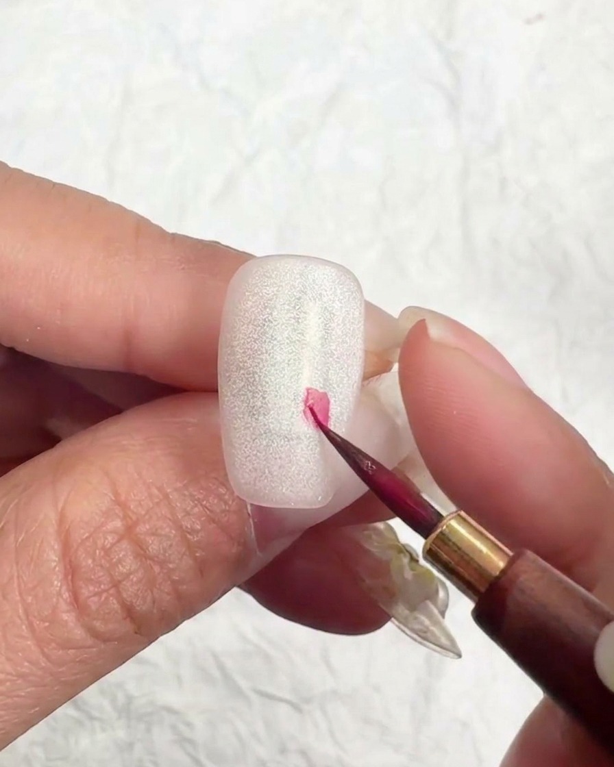 Un pennello a punta sottile posiziona un piccolo punto rosa sullunghia per iniziare un fiore di ciliegio.