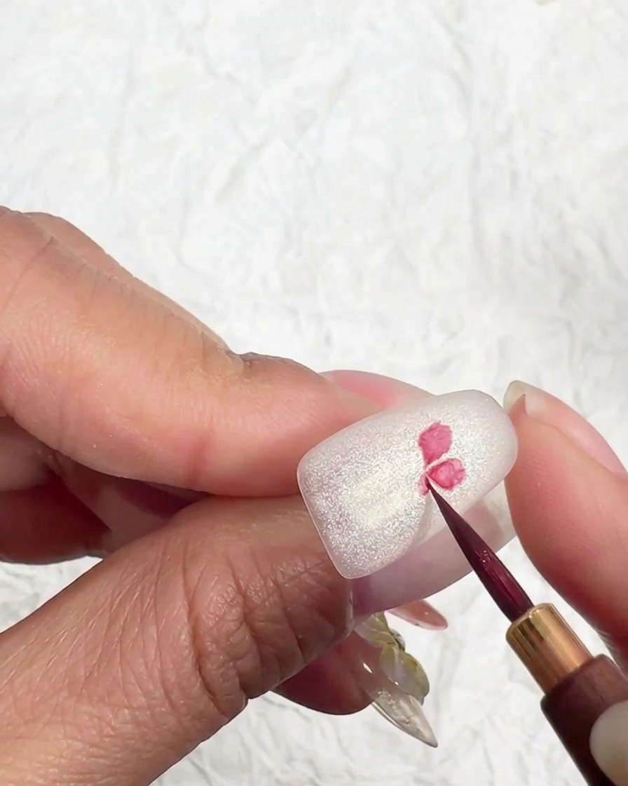 Un pennello per nail art sottile dipinge il centro di un fiore di ciliegio rosa su una superficie opaca.