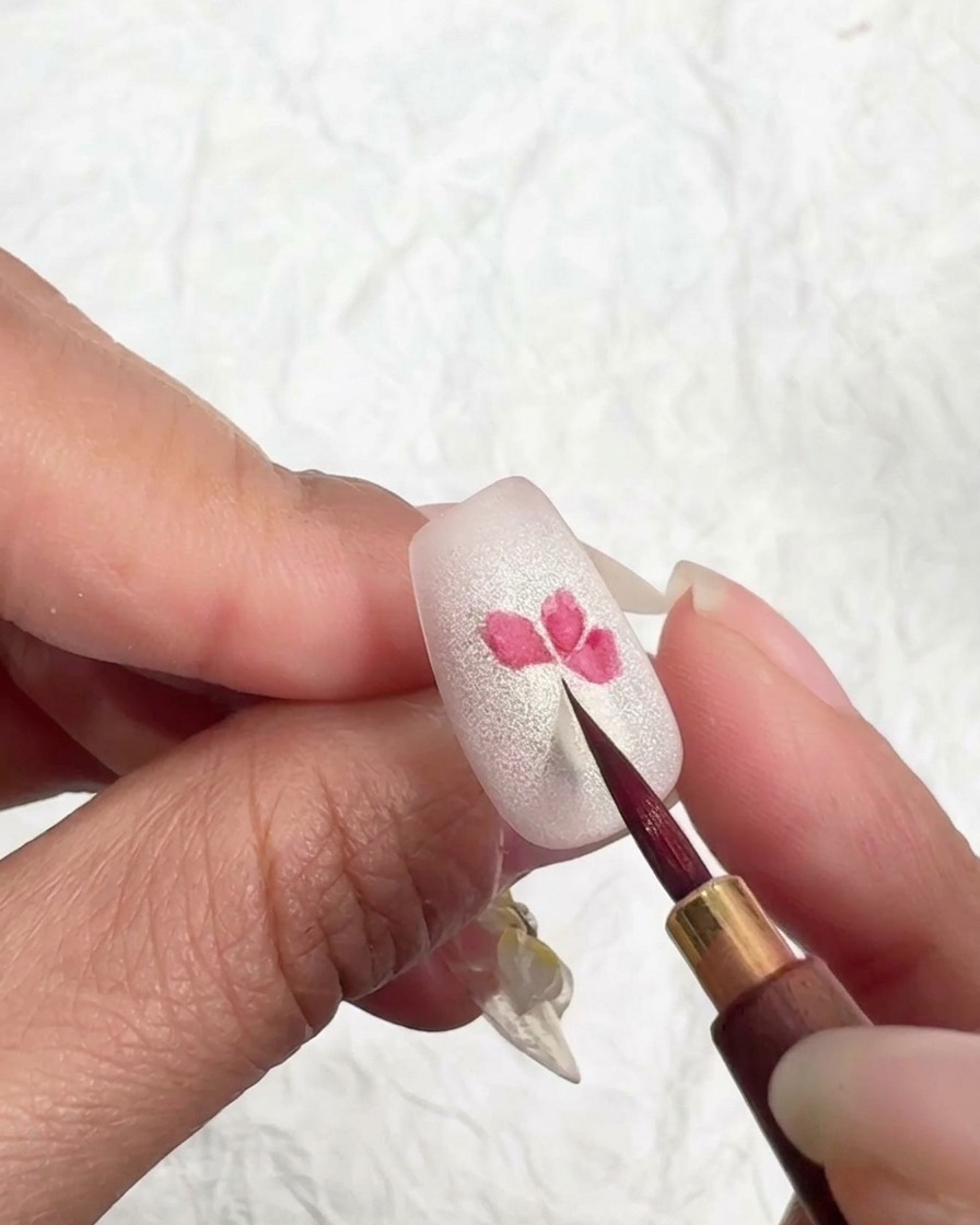 Un pennello pulito tocca leggermente i bordi di un petalo rosa su ununghia per ammorbidire e sfumare il colore.