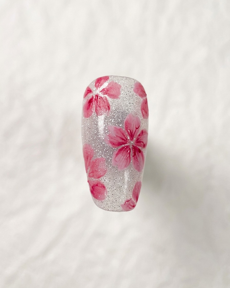 Dettaglio ravvicinato di una nail art a fiore di ciliegio completata, evidenziando i dettagli scuri e sottili al centro dei fiori.