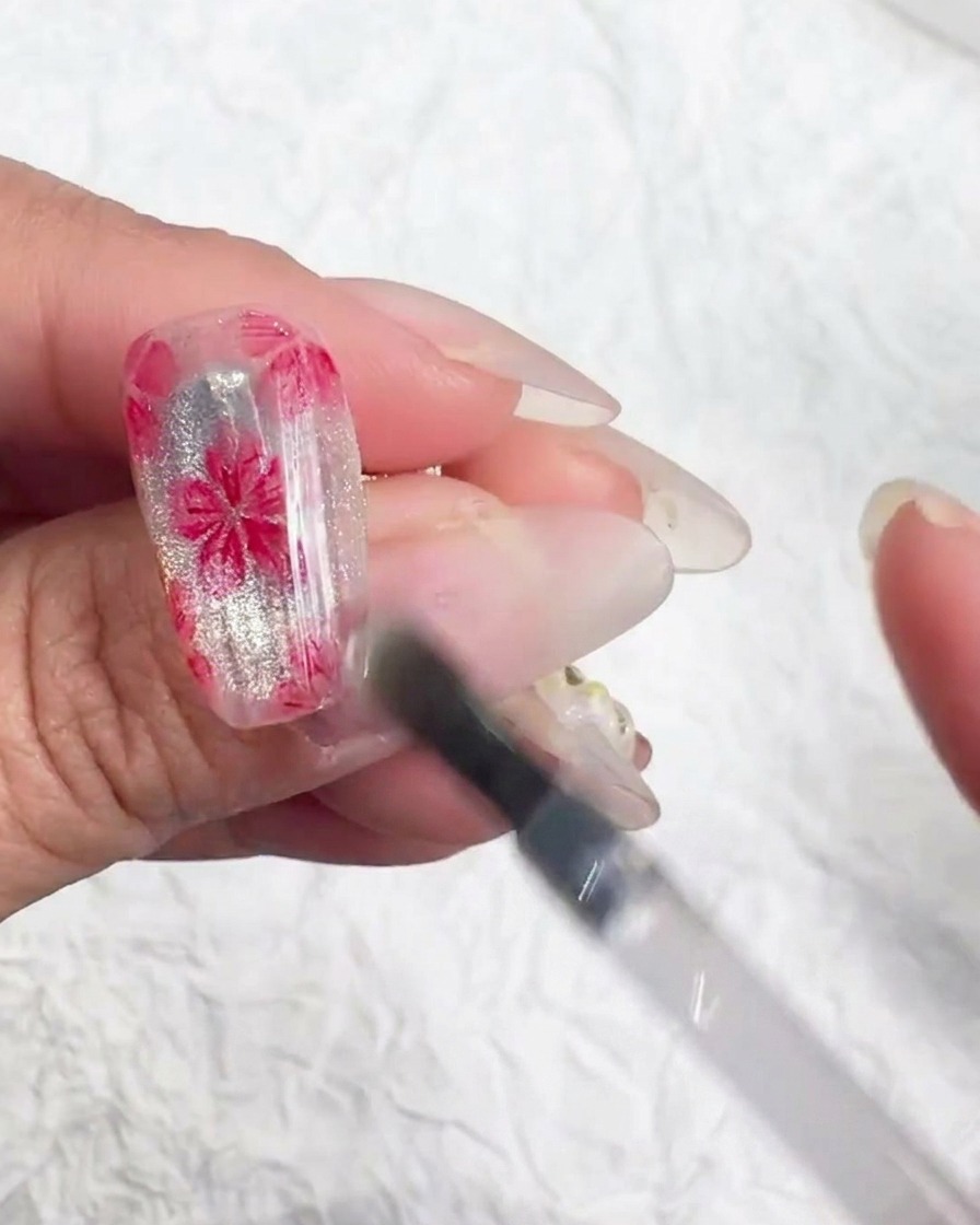 Uno strumento per nail art applica minuscole scaglie iridescenti al centro di un fiore di ciliegio dipinto.