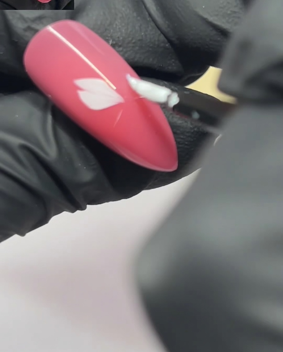 Un pennello per nail art applica un secondo petalo accanto al primo su ununghia rosa.