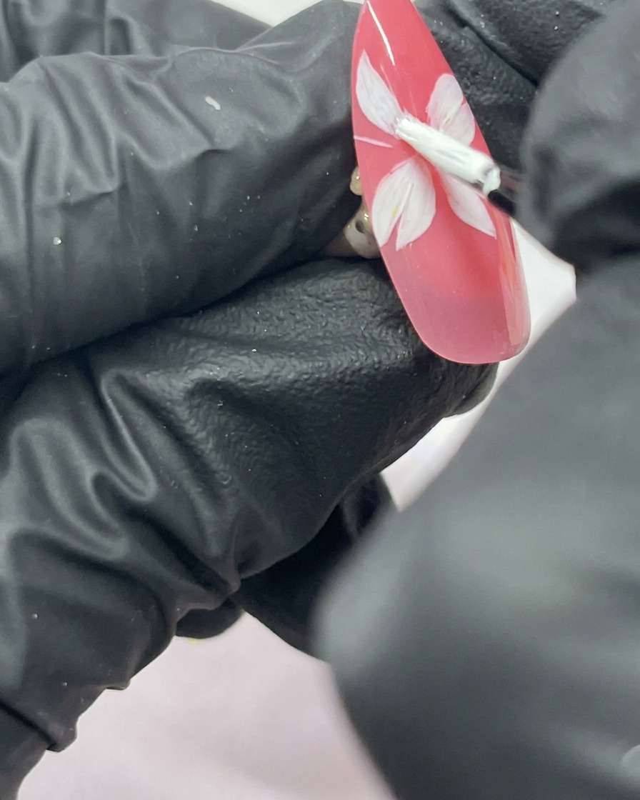 Primo piano di ununghia con un fiore di ciliegio bianco a cinque petali dipinto su uno sfondo rosa.