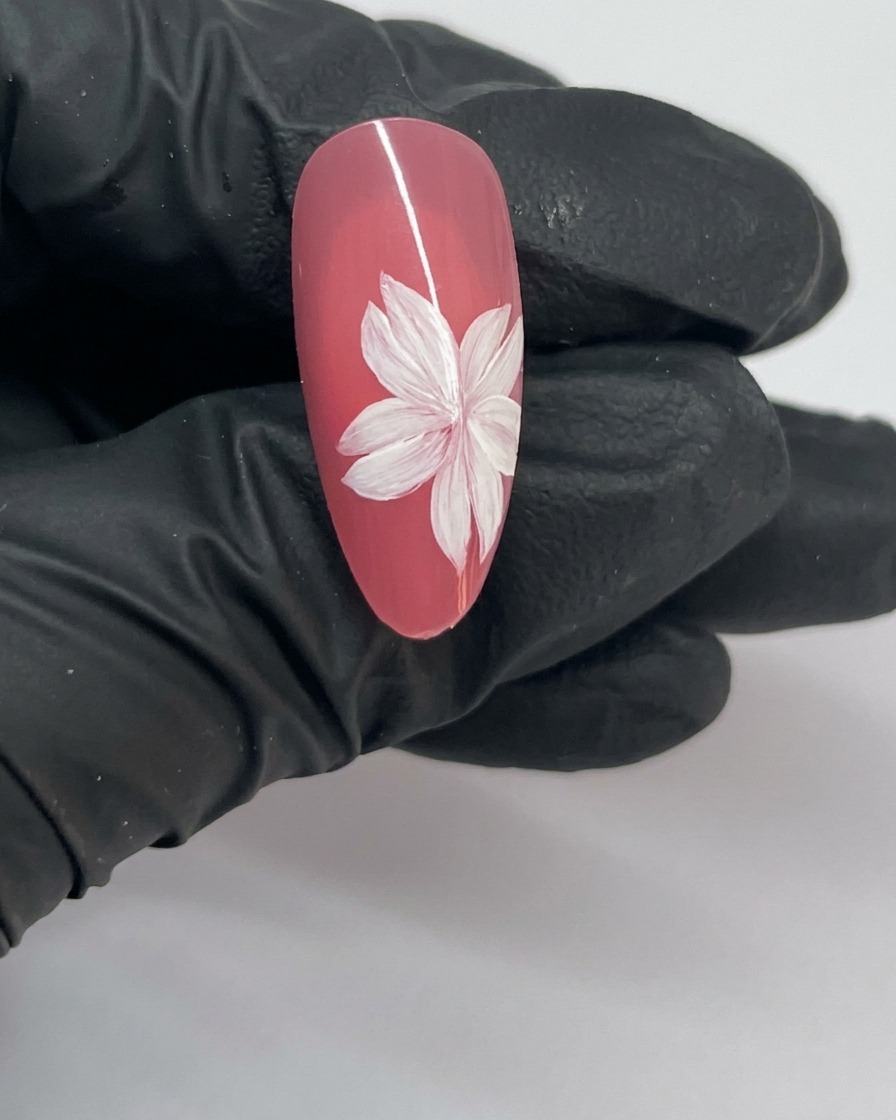 Primo piano di una nail art con fiori di ciliegio finita, che mostra un fiore completo con stami bianchi al centro.