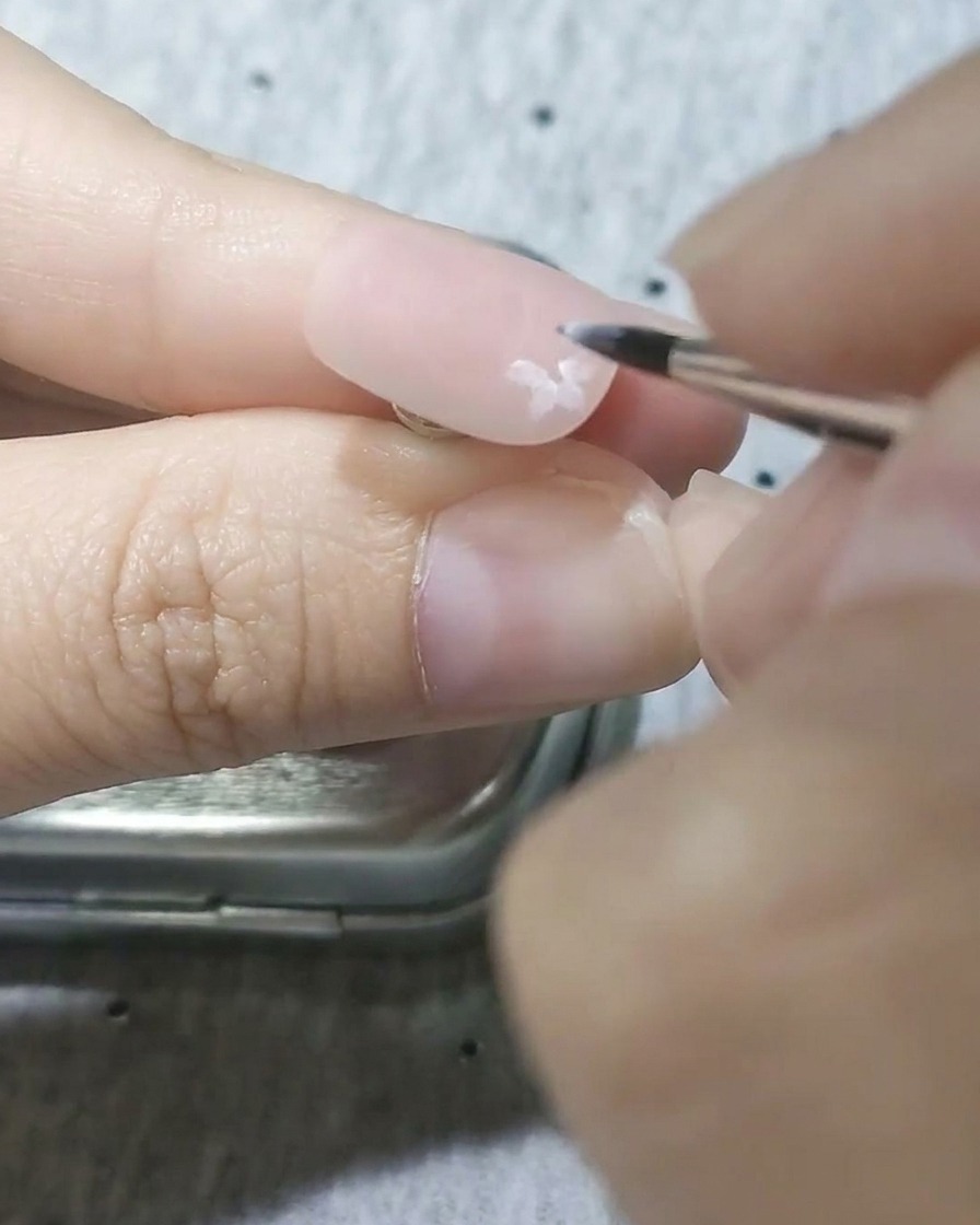 Primo piano di un pennello di precisione che dipinge petali bianchi semitrasparenti su una base rosa opaca.