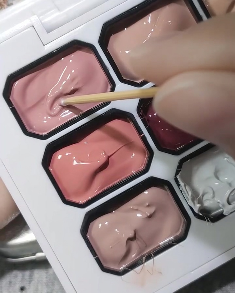 Stuzzicadenti di legno che immerge in una tavolozza di gel rosa ciliegio coprente.