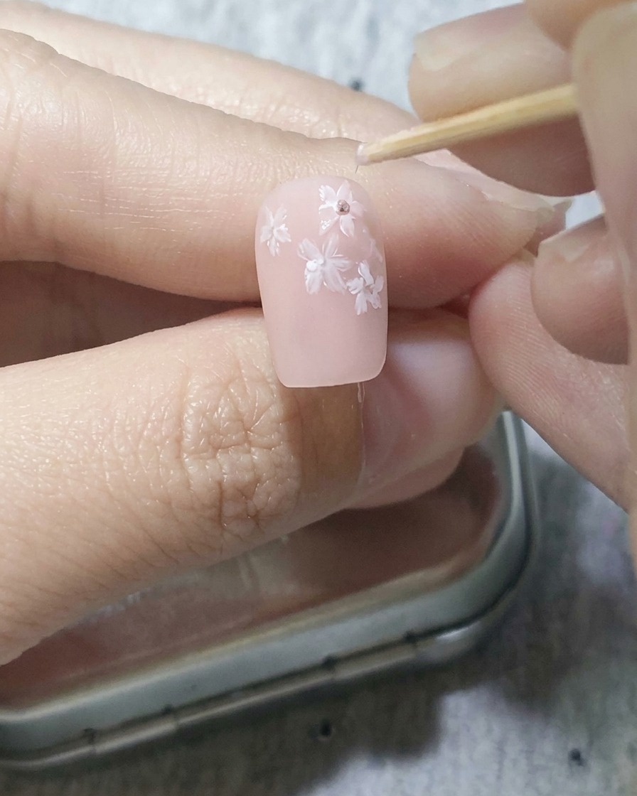 Uno stuzzicadenti che posiziona delicatamente punti rosa scuro al centro dei fiori dipinti su una base rosa tenue.