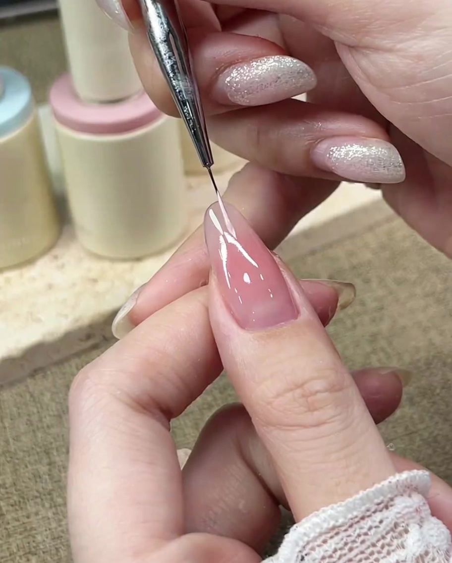 Pennello a punta fine che disegna la curva sinistra della linea del sorriso del French con gel rosa pastello.