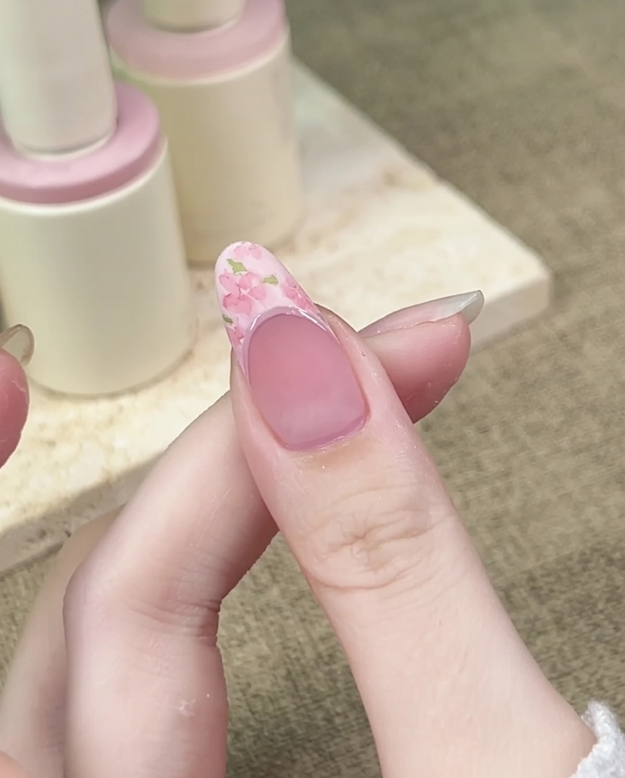 Pennello liner sottile che aggiunge piccole foglie verdi attorno ai fiori rosa sulla superficie dellunghia.