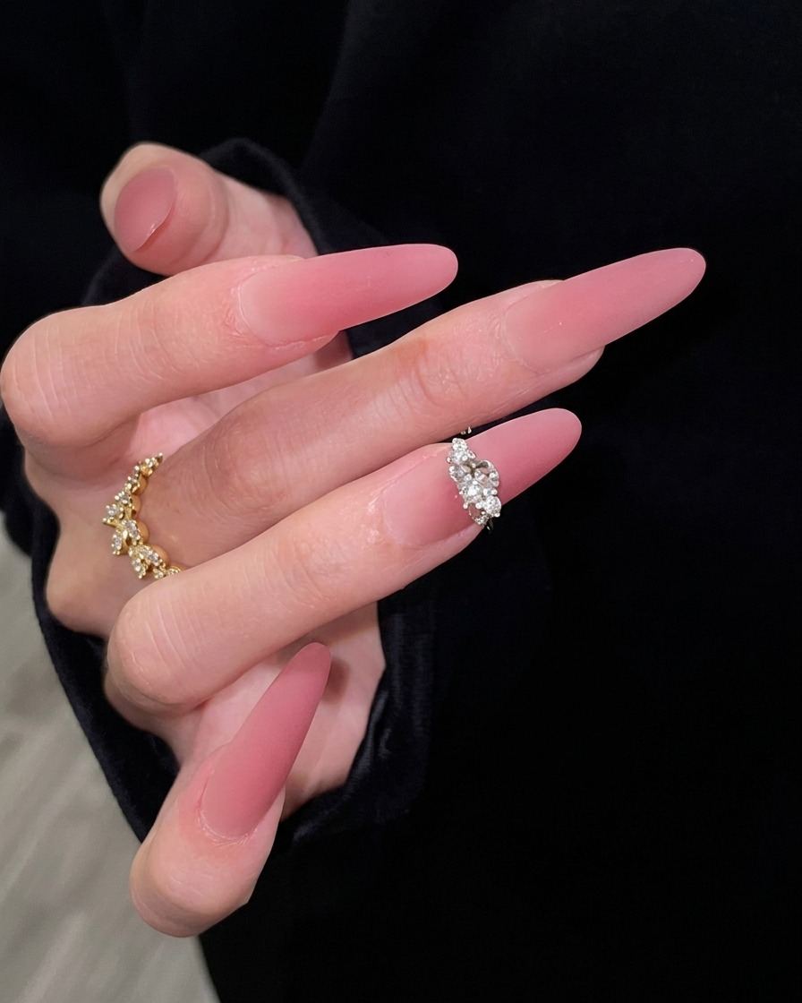 Una mano con lunghe unghie sfumate rosa in posa elegante contro uno sfondo scuro, che mette in risalto la transizione perfetta dal nude traslucido al rosa scuro.