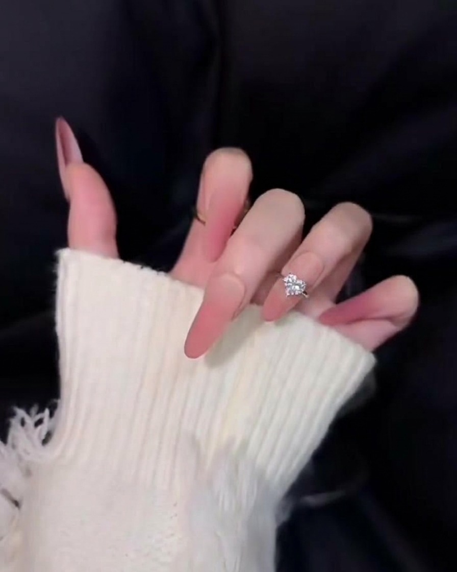 Primo piano di unghie lunghe ombré rosa splendidamente affusolate su sfondo nero, che mostrano una finitura morbida e diffusa simile al velluto.