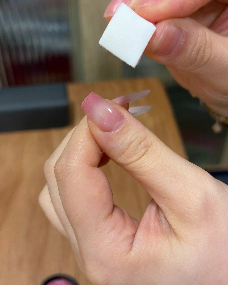 Un primo piano che mostra una spugnetta che picchietta il gel rosa su ununghia, creando un delicato effetto sfumato dalla punta verso il centro.