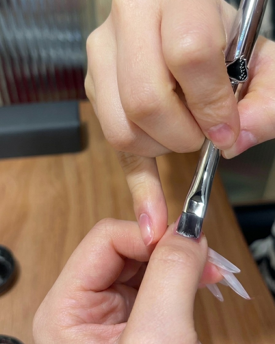 Un pennello piatto che applica uno strato sottile di gel cat-eye scintillante su ununghia con una sfumatura rosa preesistente.