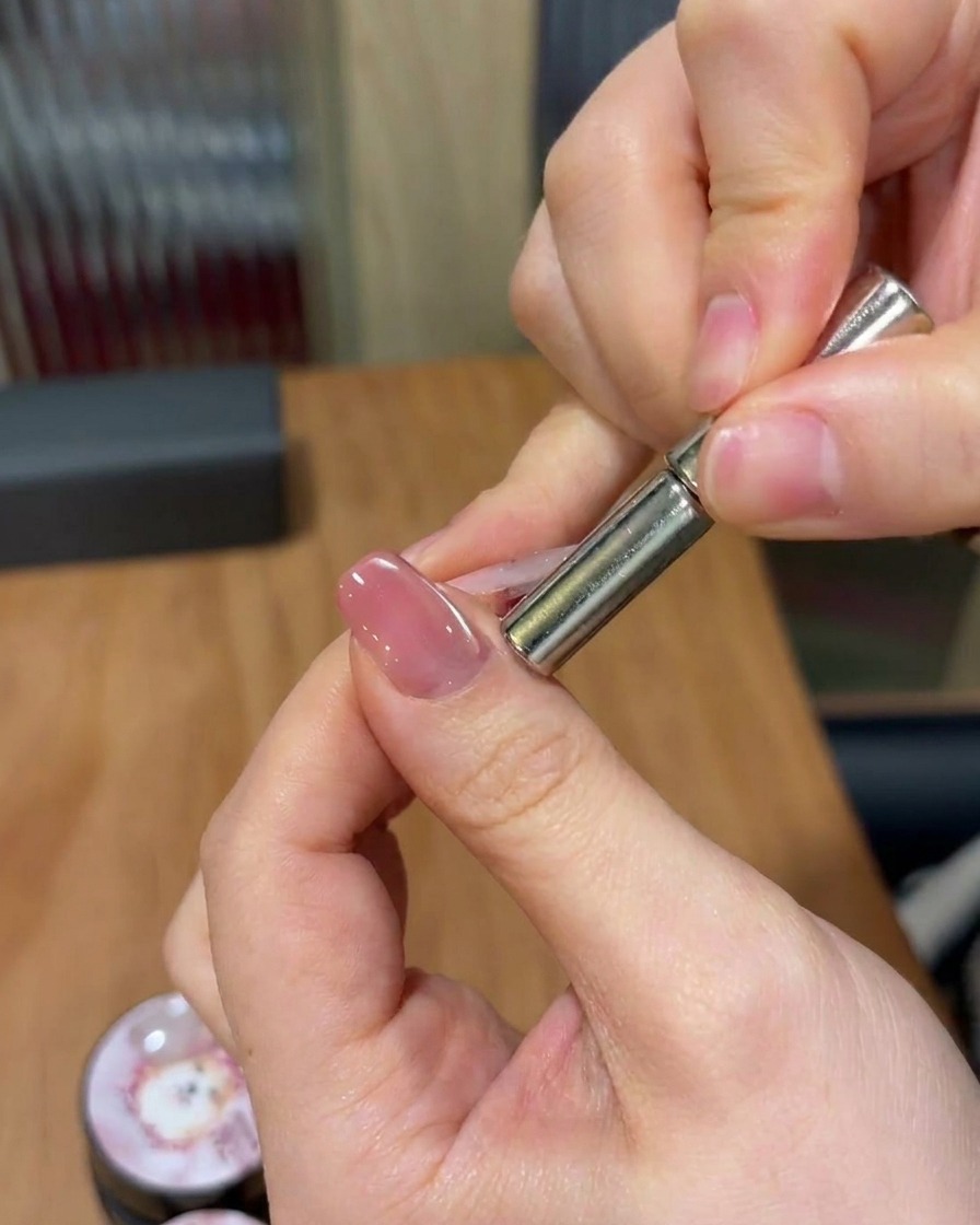 Una mano che tiene un magnete cilindrico sopra ununghia, muovendolo per manipolare le particelle magnetiche in una banda scintillante diagonale.