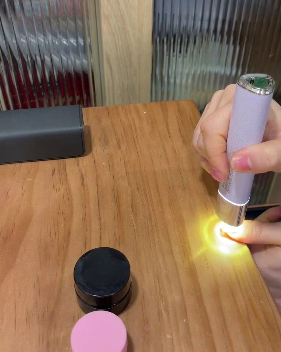 Un dito posizionato sotto una piccola lampada LED portatile viola su un tavolo di legno, che polimerizza lo smalto gel.
