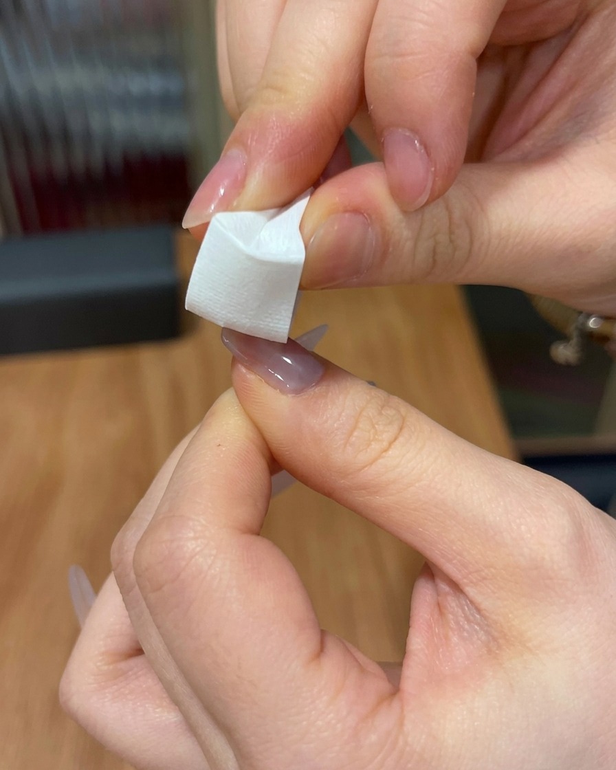 Un primo piano di una spugnetta usata per tamponare il gel rosa sulla punta di ununghia.