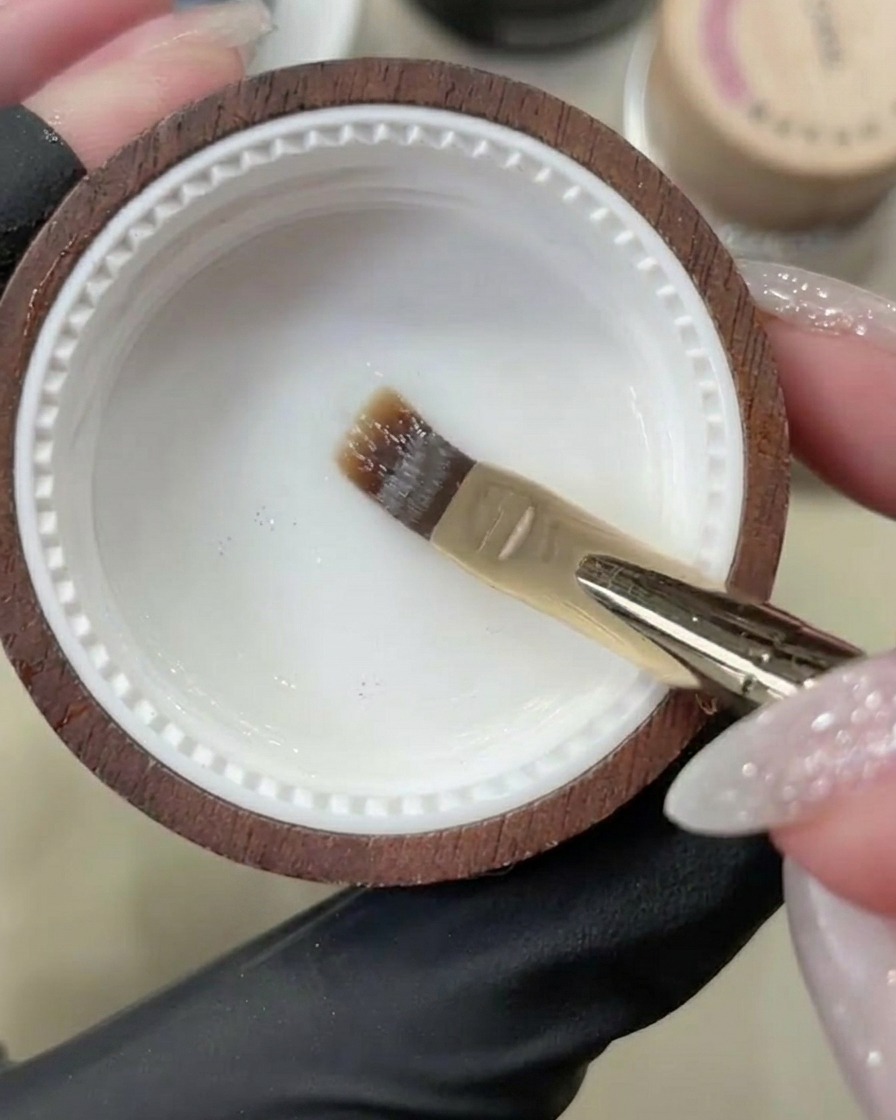 Un pennello da gel applica una base coat trasparente su ununghia naturale pulita.