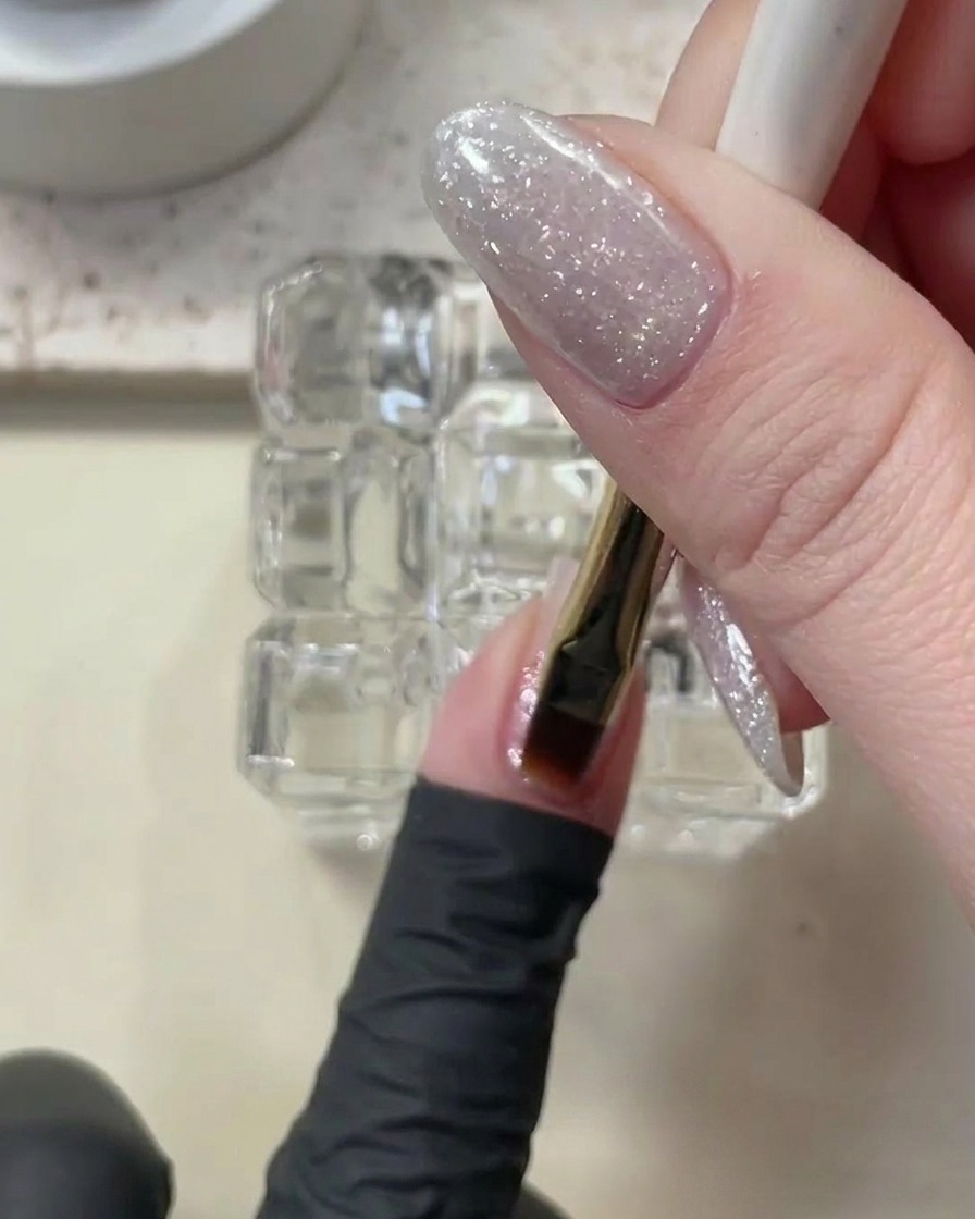 Un pennello che applica uno strato sottile di gel costruttore trasparente su ununghia ricoperta di glitter.