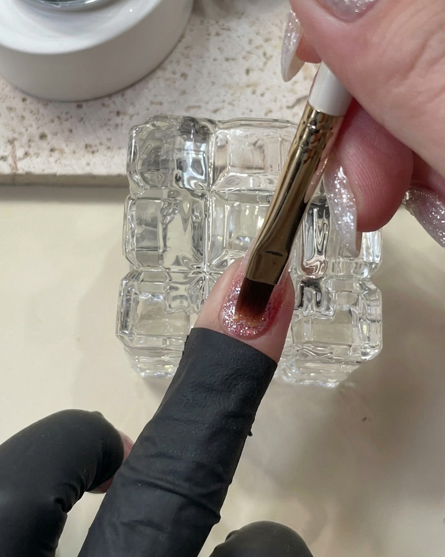 Un pennello che applica una goccia più spessa di gel costruttore autolivellante sullunghia.