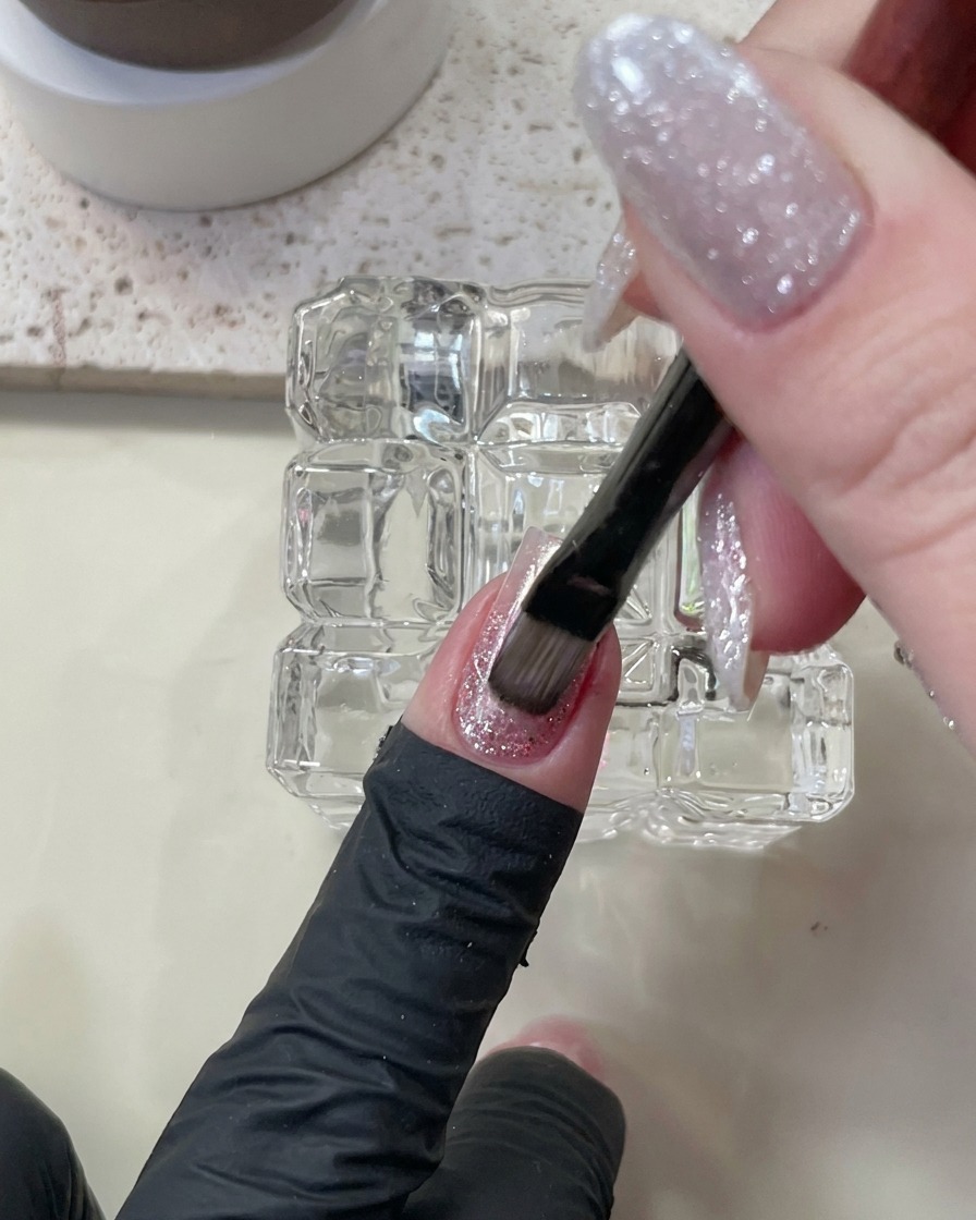 Un pennello che applica uno smalto gel cat-eye color carne sopra gli strati esistenti.