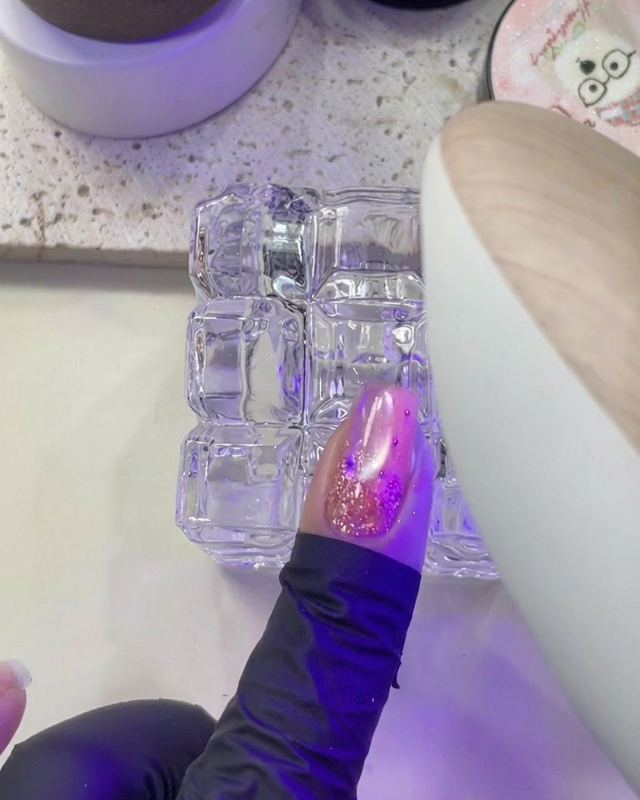 Una mano che posiziona ununghia sotto la luce viola di una lampada UV/LED per unghie per la polimerizzazione.
