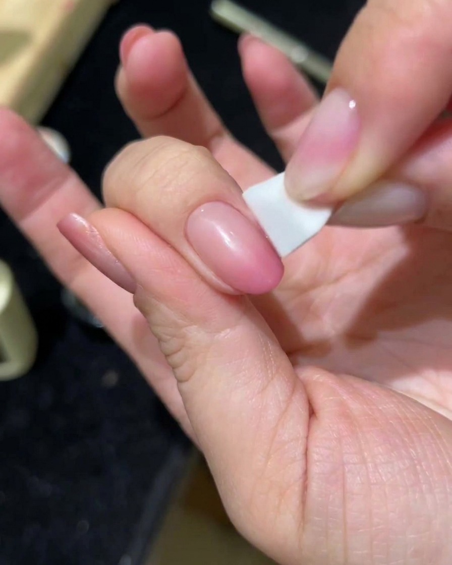 Una mano che picchietta un secondo strato di gel cat-eye rosa su ununghia usando una spugnetta.