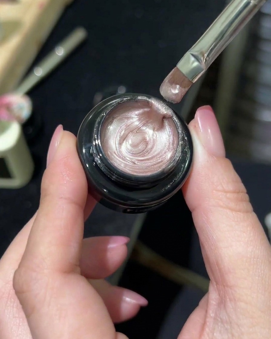 Un pennello professionale per unghie che preleva un gel magnetico scintillante effetto aurora da un vasetto.
